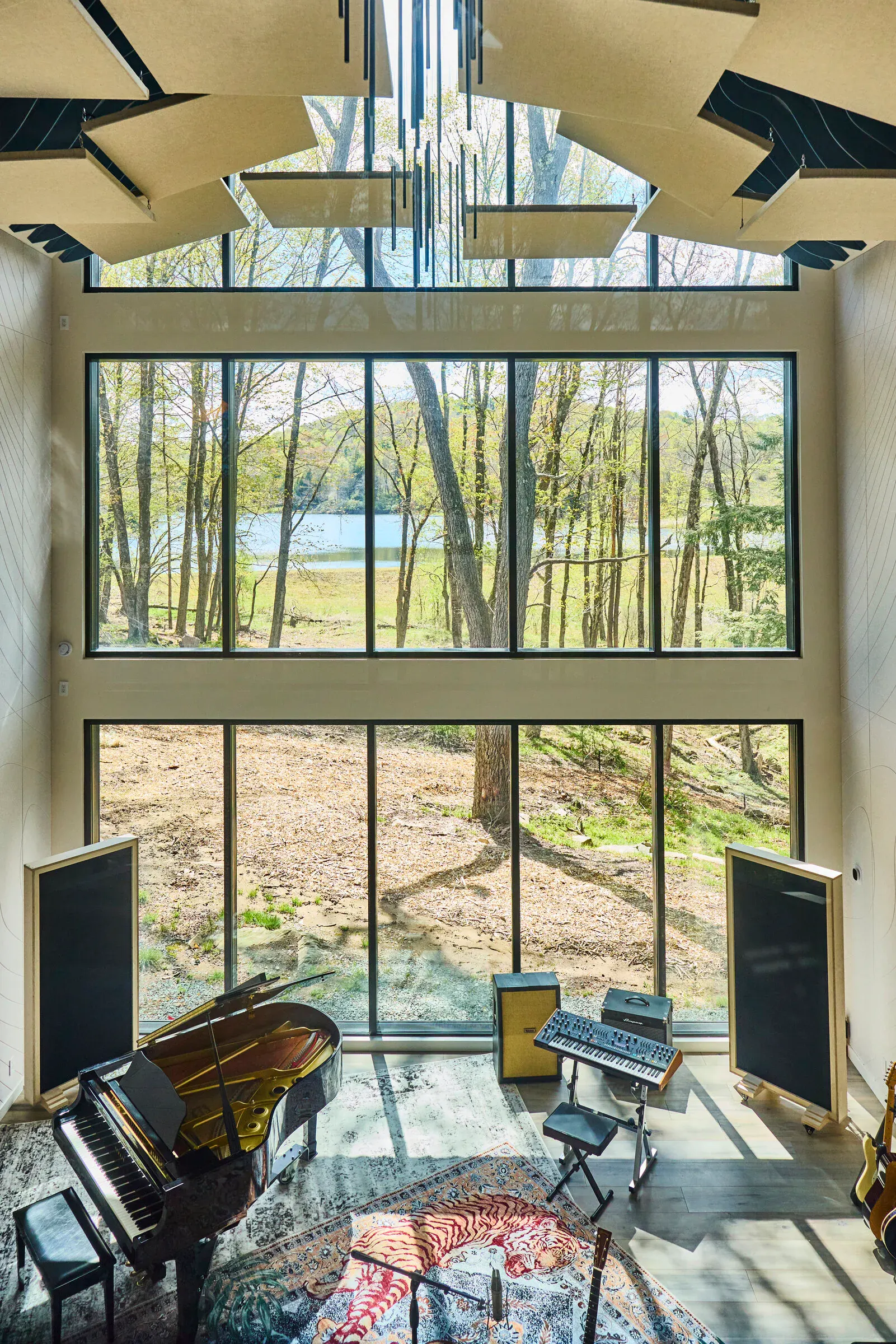 Verdant Sound live room — floor-to-ceiling glass wall overlooking the private lake, grand piano and synthesizers